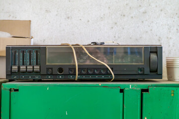 An old radio with equalizer, set on a green metal cabinet. The device looks used and slightly dusty. On the front are visible sliders, buttons. retro equipment in an abandoned factory.
