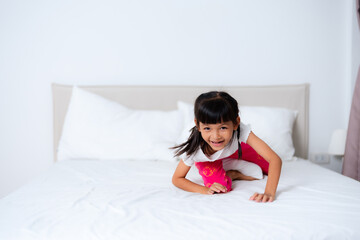 Little girl playing on bed wearing pajamas in bedroom