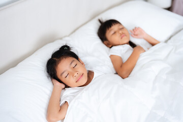 Two asian children sleeping peacefully in white bed holding hands