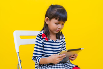 Cute asian girl using tablet while sitting on chair with yellow background