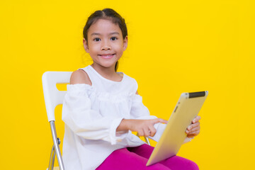 Smiling girl using digital tablet sitting on chair against yellow background