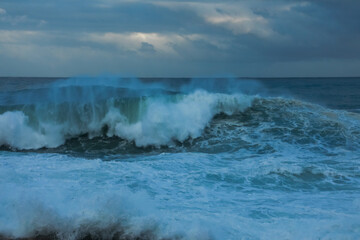 Huge foaming waves in a stormy sea with spray crashing on the coastal rocks in the evening on the Maltese coast.