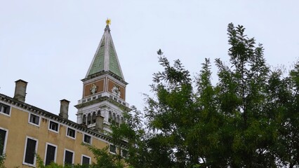 Obraz premium St. Mark's campanile towering over venetian buildings and lush green trees. Action