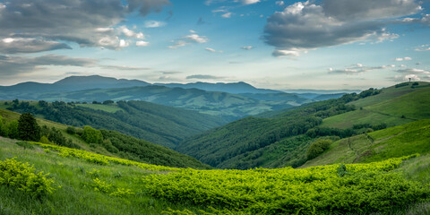 Naklejka premium Breathtaking panoramic landscape of rolling lime-green meadows, lush forested hills, and misty mountain ranges beneath a vibrant azure sky with wispy, dynamic cloud patterns