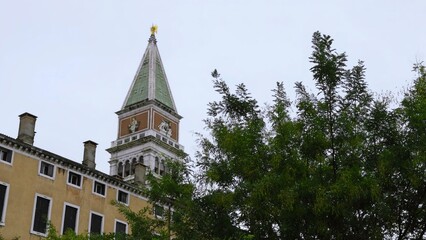 Obraz premium St. Mark's campanile towering over venetian buildings and lush green trees. Action