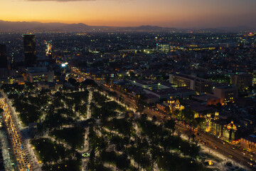 Aerial View of Mexico City at Dusk with Illuminated Streets and Distant Mountains.