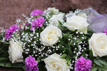 Flower arrangement of white roses and pink carnations at the grave. Beautiful grave flowers in the cemetery. Relatives want to remember the deceased with flowers. 