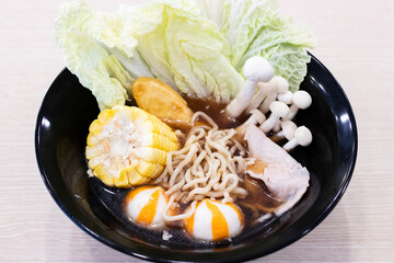 Noodle soup in a sleek black bowl There are curly noodles, sweet corn, crisp napa cabbage leaves, slices of pork, golden fish tofu, white shimeji mushrooms.