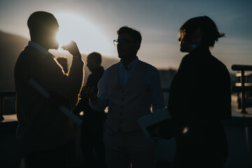 A group of diverse business people engages in brainstorming on a high rise balcony at sunset,...
