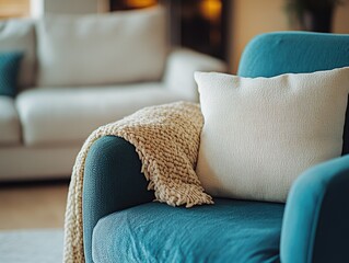 This image showcases a comfortable living room setting, featuring a teal blue sofa adorned with two throw pillows. The sofa is accompanied by a soft, knitted blanket draped over one armrest,