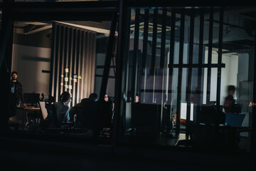 A diverse team of professionals working late at night in an office. They are engrossed in brainstorming sessions, discussions, and strategic planning to meet important deadlines.