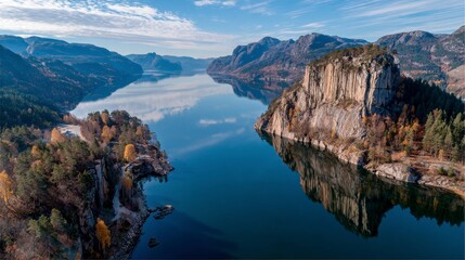 Panoramic view of a calm lake nestled between steep, rocky hillsides, showcasing autumn foliage and clear reflections.