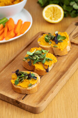 Delicious bruschetta with pumpkin hummus and microgreens on wooden board
