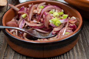 Pickeld red sliced onion in clay dish on wooden table