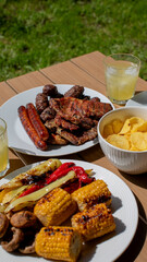 Barbecue feast with grilled meats, vegetables, and drinks on a sunny day, perfect for summer picnics or Fourth of July