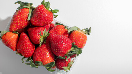 Fresh strawberries in clear container on white surface, summer fruit harvest, healthy eating, freshness, picnic dessert idea