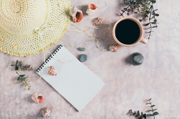 Travel planning notebook, hat, seashells and cup of coffee on table top view