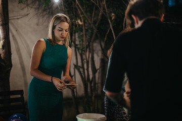 Woman in an elegant green dress engages in activities at an outdoor evening gathering. The ambiance...