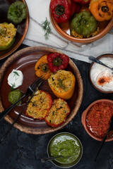 Vegan stuffed peppers with rice, corn grits, vegetables and herbs on clay servingware with side dishes, copy space