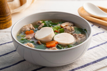 Clear Ivy gourd soup with minced pork and soybean tofu in white bowl on wooden table,Thai food.(gaeng jued tum luang)