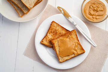 Toast bread and Homemade peanut butter.Spreading peanut butter on slice whole wheat bread in white plate.Top view