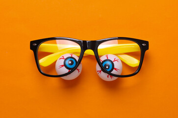 Eyeballs with eyeglasses on orange background. Minimalism halloween still life