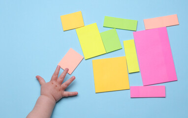 Kids hand holding blank paper multicolored stickers. Sticky note collection on blue background