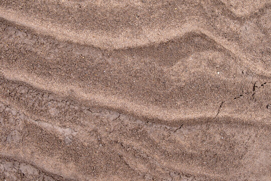 Sandy dark brown background, texture. River beach close-up, silt sandy soil. Abstract wavy surface.