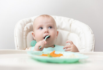Cute baby eating healthy food at feeding table