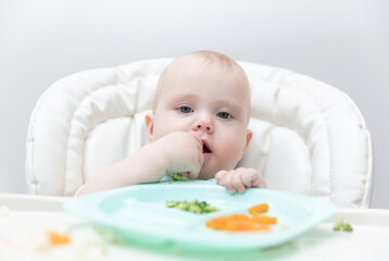 Cute baby eating healthy food at feeding table