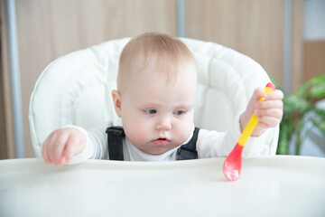 Cute baby with spoon sitting at feeding table