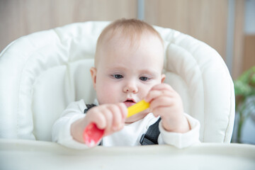 Cute baby with spoon sitting at feeding table