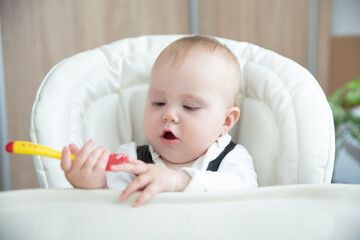 Cute baby with spoon sitting at feeding table