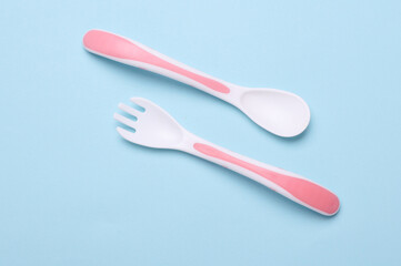 Plastic fork and spoon for feeding baby on blue background