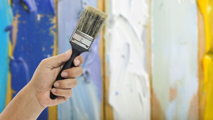 Hand holding a paint brush against a colorful wooden background for creative projects