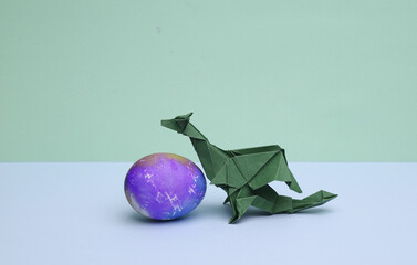 Origami dragon with colored egg on a pastel background. Conceptual easter photo