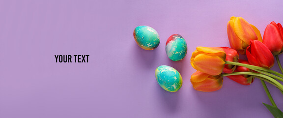 Multicolored Easter eggs with tulips on purple background. Space for your text. Top view