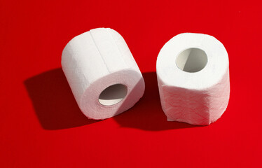 Two rolls of white toilet paper on a red background with a shadow