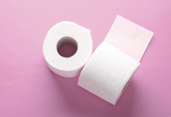 Two rolls of white toilet paper on pink background with a shadow