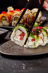 Chef using chopsticks holding uramaki sushi rolls with chuka seaweed, shrimp, cream cheese and tobiko red caviar