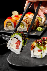 Woman holding uramaki sushi roll with chopsticks over black plate