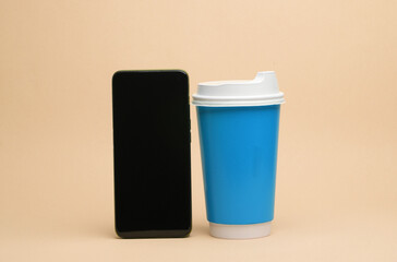Disposable coffee cup with smartphone on beige background