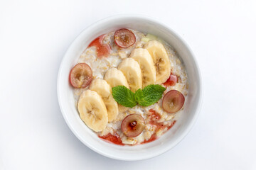 Oatmeal porridge with banana and grape in bowl on white background
