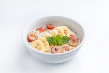Oatmeal porridge with banana and grape in bowl on white background