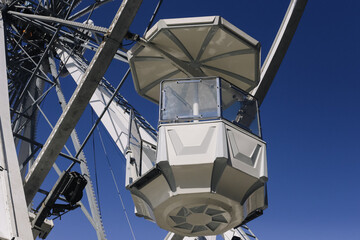 White ferris wheel cabin. Amusement park attraction. Fun fairground ride. Clear blue sky. Modern metal structure. Bright sunny day. Leisure and joy. Holiday adventure concept. © Paweł Michałowski