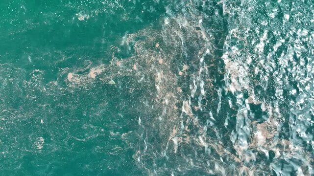 The aerial shot reveals a stretch of ocean marred by scattered marine debris, showing the widespread nature of plastic and waste pollution in our seas.
