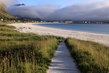 Landscape photo with a view of mountains partially covered by clouds and Ramberg Beach late in the evening during the "white nights" in the Lofoten Islands in Norway