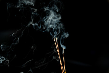 Three burning incense sticks with smoke on a black background.