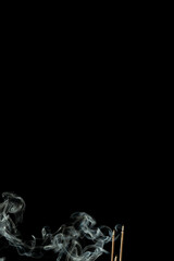 Three burning incense sticks with smoke on a black background.