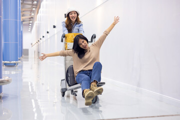 Riding baggage trolley. two Happy Asian beautiful woman passenger traveler and friends having fun with luggage at the airport
